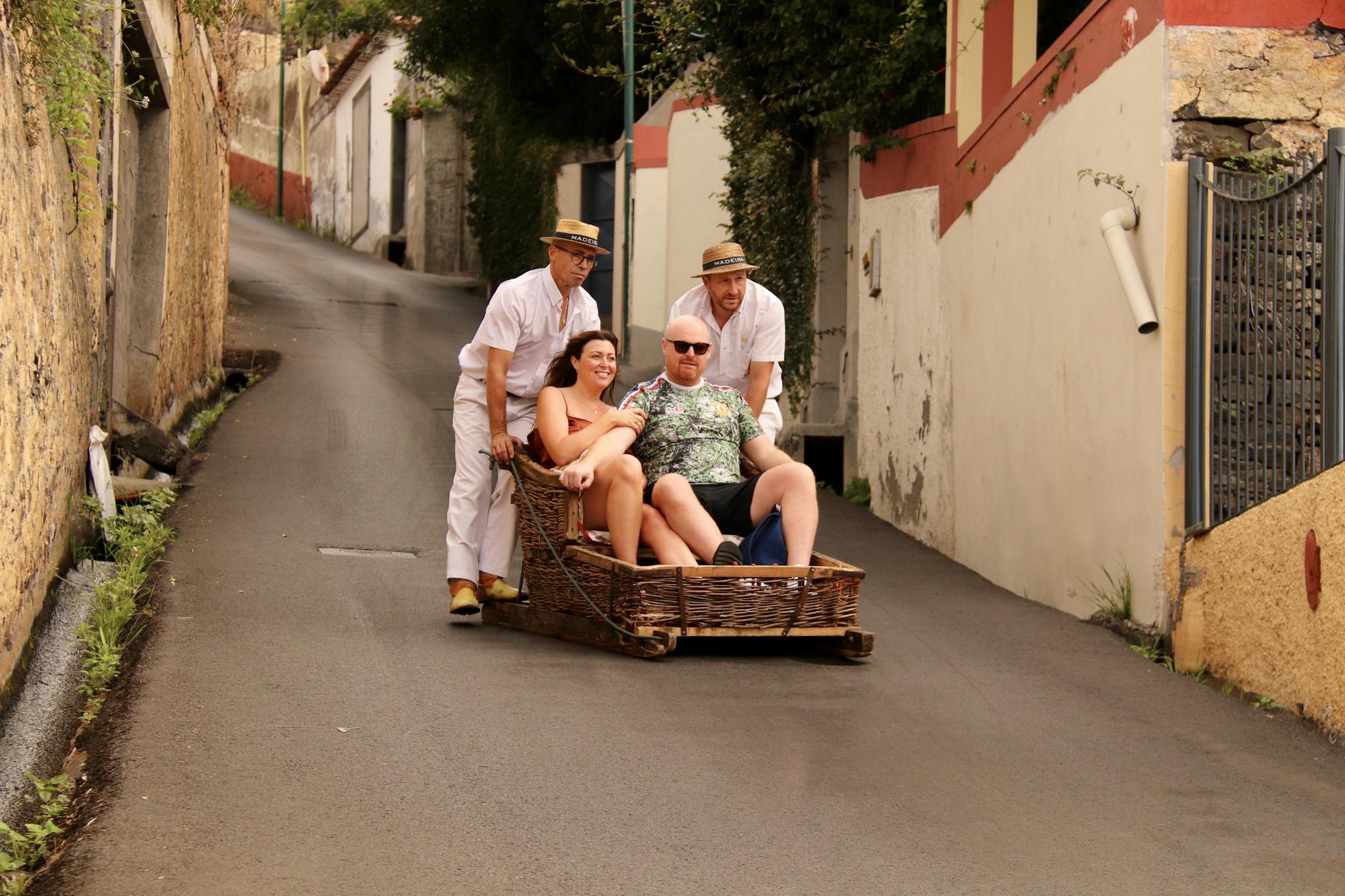 Tourists enjoying a classic toboggan ride down the steep streets of Funchal, Madeira.
